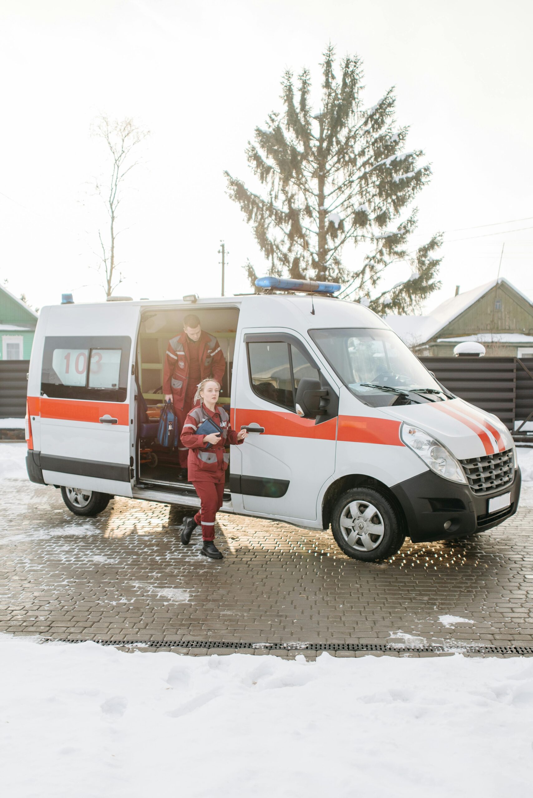 Paramedics stepping out of an ambulance with equipment on a snowy outdoor scene.