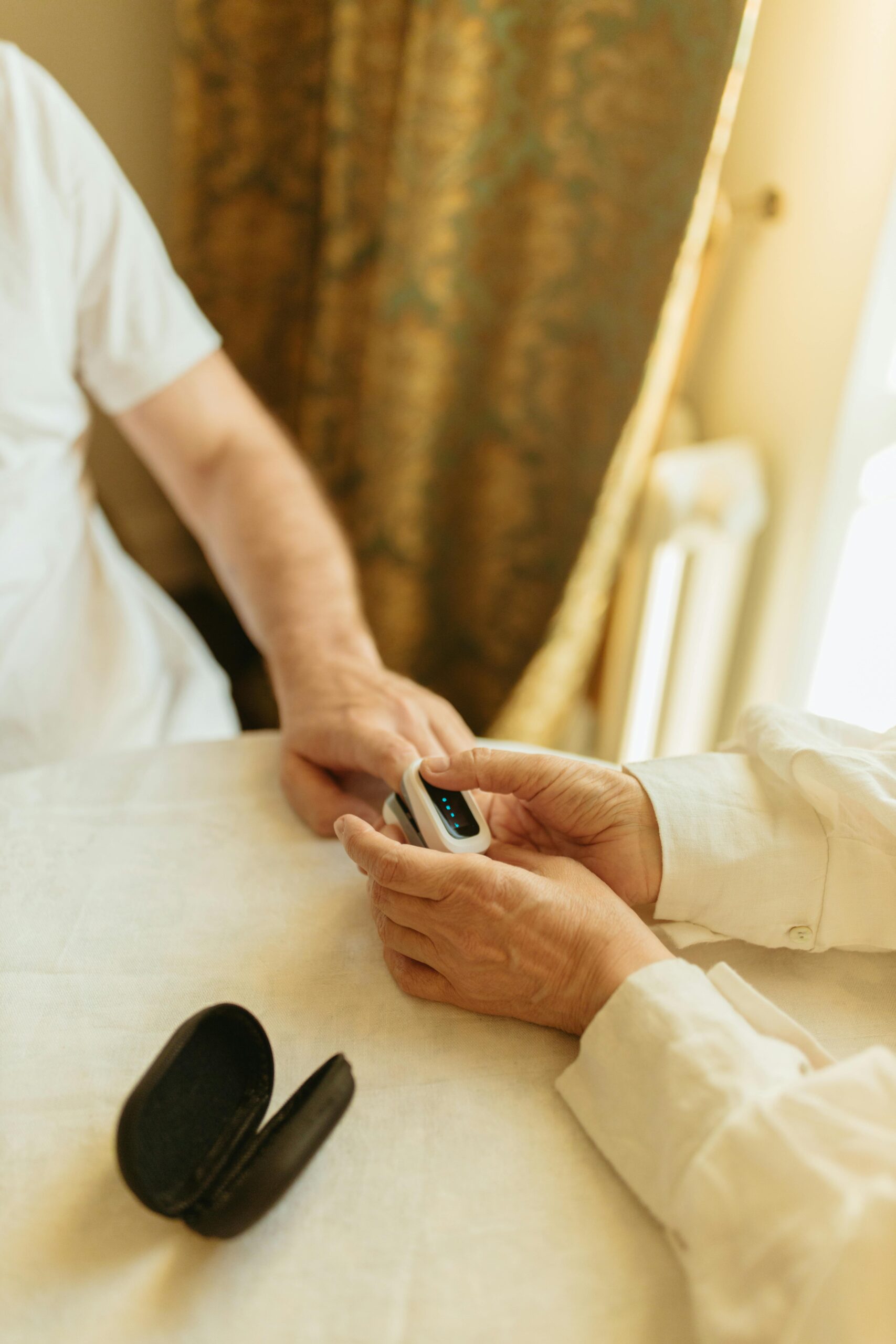 A senior adult using a pulse oximeter indoors to monitor health in a warmly lit room.