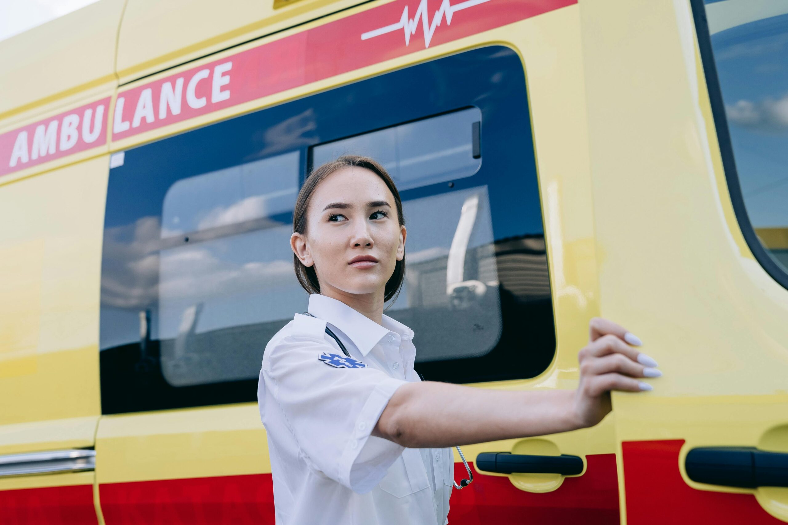 A focused paramedic in uniform standing beside a bright yellow ambulance.