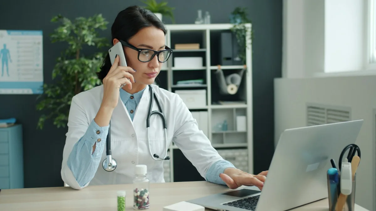 Healthcare professional on a phone call while working on a laptop in a clinic office, as PMHNP recruiters do when arranging a placement