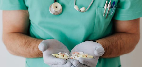 A healthcare professional in uniform holding a variety of pills in gloved hands.