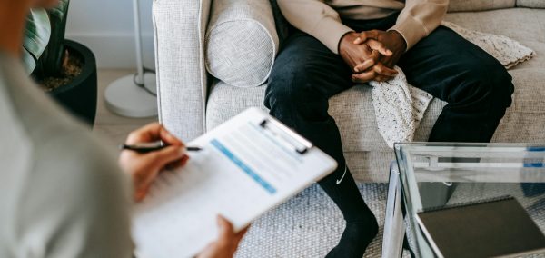 Therapist takes notes as client sits on a sofa during a psychotherapy session.