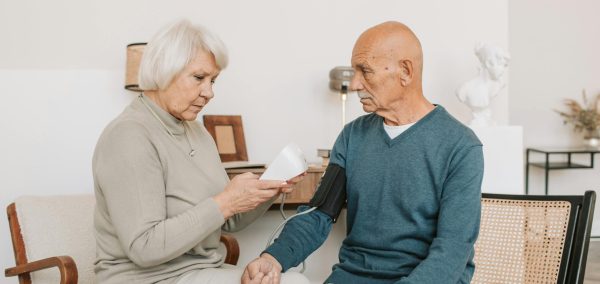 Senior couple measuring blood pressure at home, showcasing care and companionship.